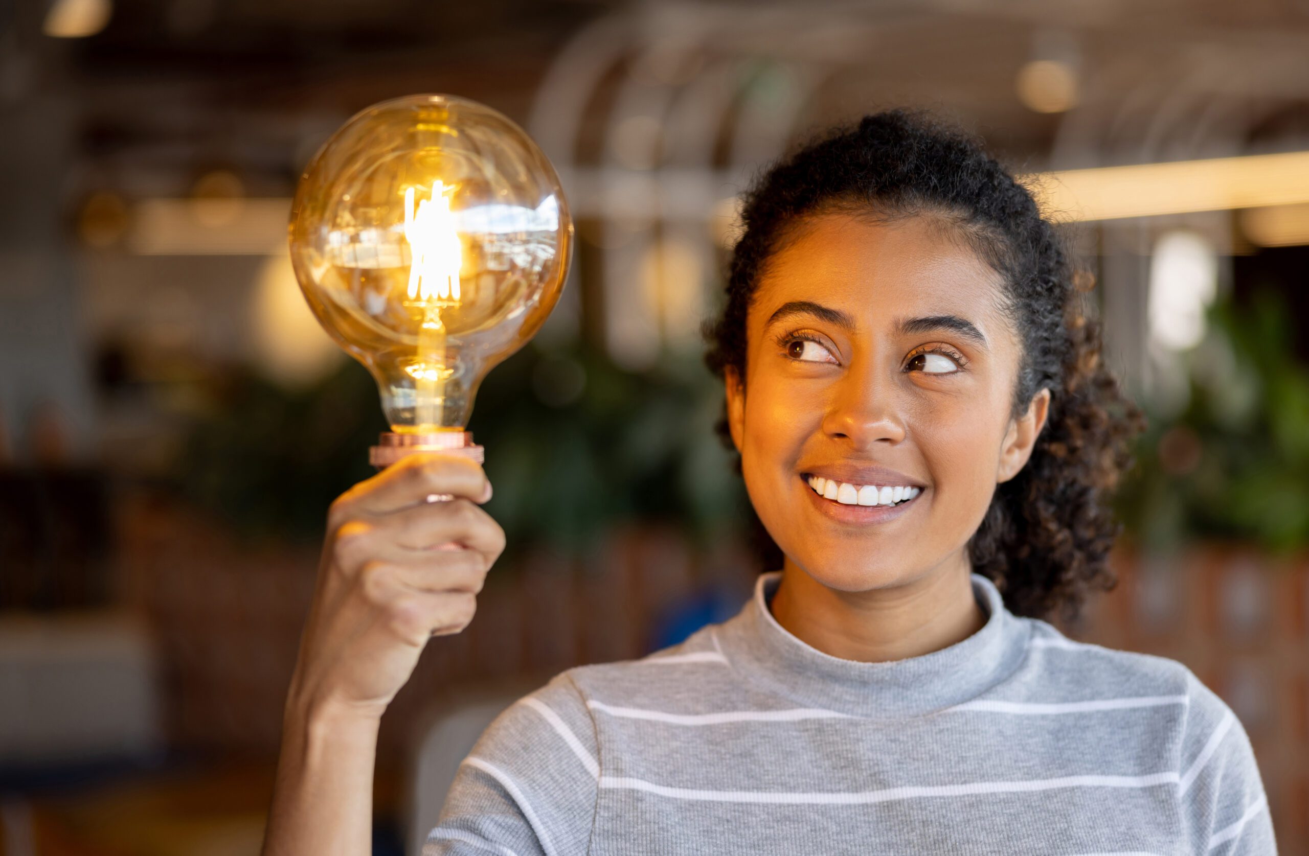 A smiling woman holding up a lit lightbulb